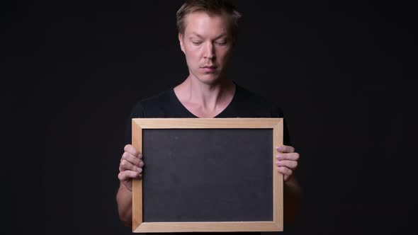 Young Handsome Man Holding Blackboard Against Black Background