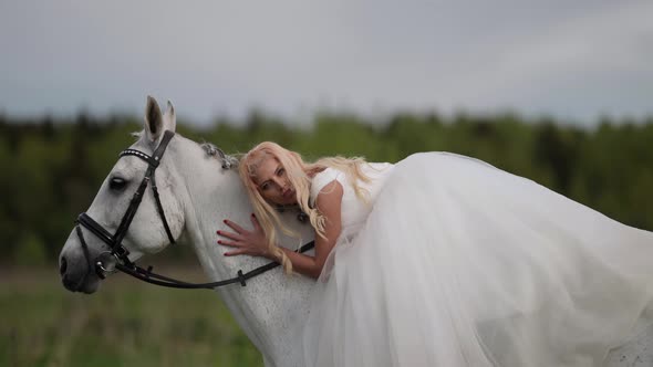 Happy Beautiful Bride is Riding White Horse at Summer Meadow Romantic Wedding Day