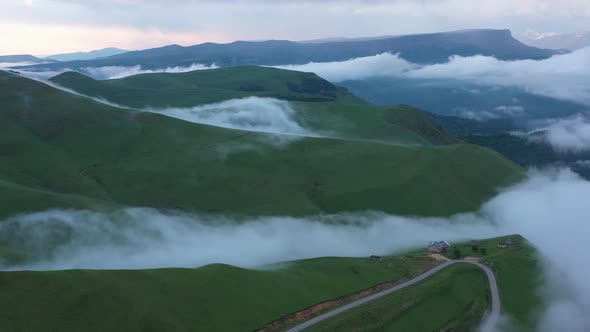 Drone Flight above green fields at the mountains in the clouds and fog.