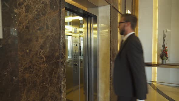 Young Man in Suit Carrying a Suitcase Walking Down the Hotel Lobby and Man Enters in the Elevator