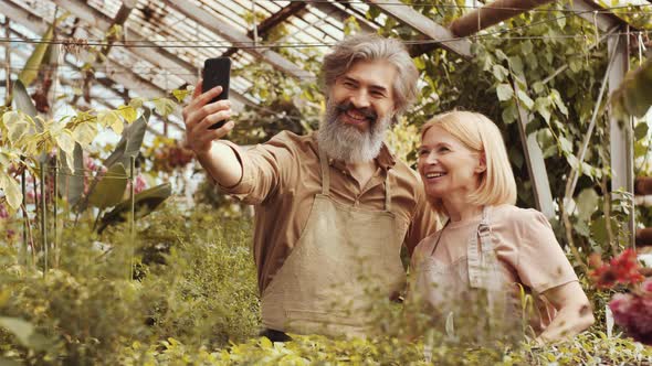 Happy Senior Couple Speaking on Web Call on Smartphone in Greenhouse Farm