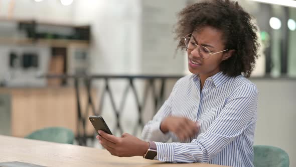 Upset African Businesswoman Reacting To Loss on Smartphone in Office 