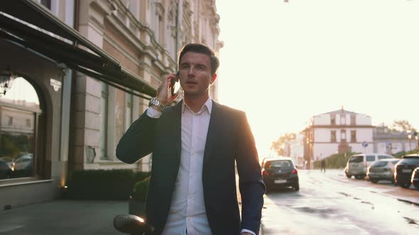 Handsome Young Stylish Man Talking on Mobile Phone Outdoors with Bicycle in City Center During