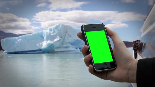 Hand holding an Old Smartphone with Green Screen near an Iceberg.