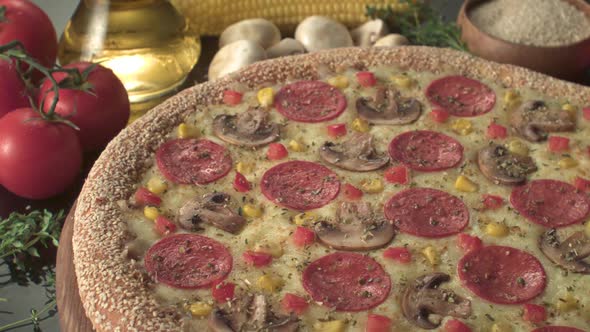 A cooked sesame crust pizza with salami, mushroom, tomato and mozzarella on a wooden plate