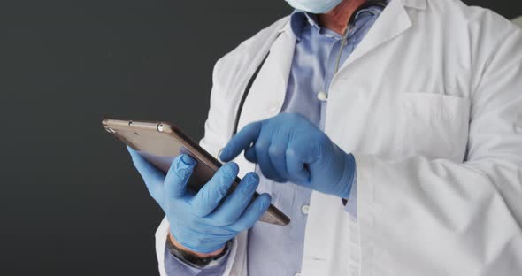 Mid section of caucasian male doctor wearing surgical gloves using digital tablet