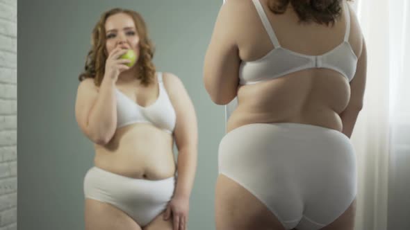Plus-Size Lady Eating Apple in Front of Mirror, Enjoying Results of Healthy Diet