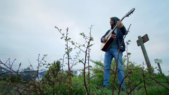 A man is playing the guitar under a moody sky outdoors