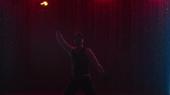 Male Fire Tamer in a Thrilling Close-up Fire Show in a Dark Studio in the Rain. A Silhouette