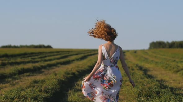 Young Attractive Redhead Woman in a White Dress Runs Away Across the Field