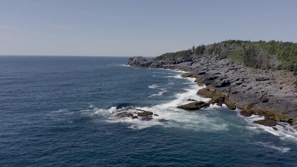 Drone flyine low along the water as a big wave crashes on the rocky coastline in Maine