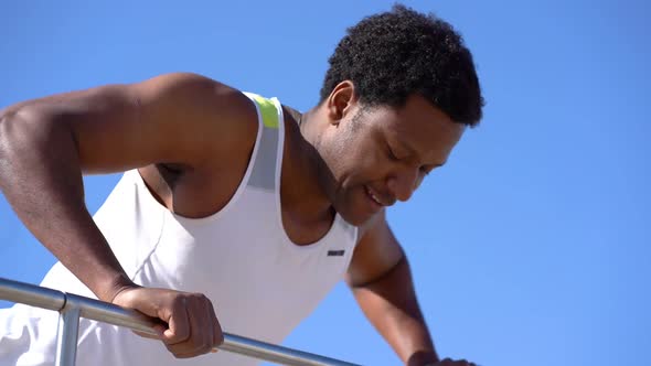 Smiling Sporty Man Training on Railing Against Blue Sky