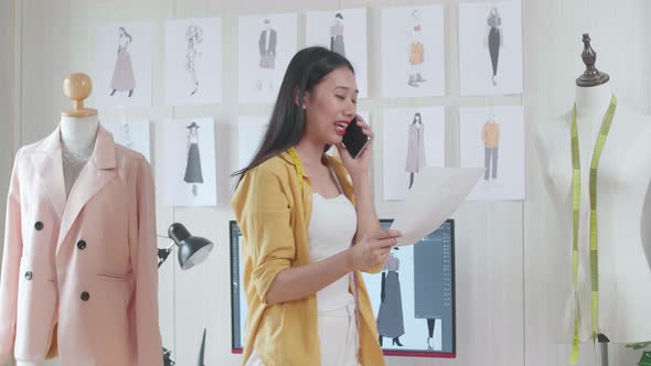 Female Designer With Sewing Machine Talking On Smartphone, Looking At Picture In Hand And Walking