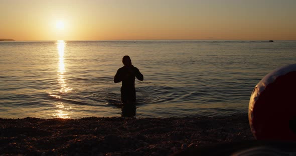 boy silhouette with wetsuit coming out of the sea at sunset
