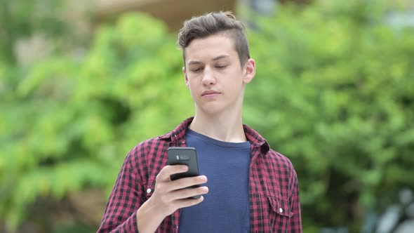 Young Happy Teenage Boy Using Phone Outdoors
