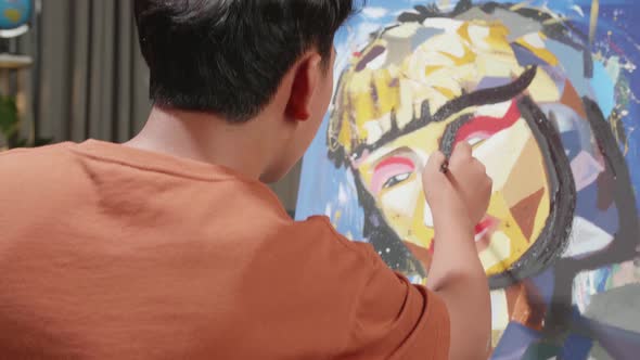 Hind View Of An Asian Artist Boy In Wheelchair Holding Paintbrush And Painting On The Canvas