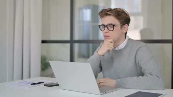 Young Man Thinking While Working on Laptop in Modern Office