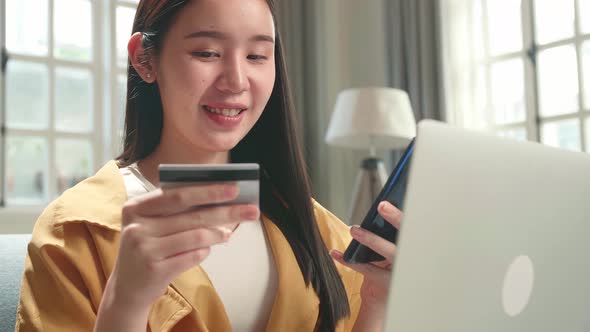 Woman Sitting On Couch And Holding Credit Card While Using Smartphone And Laptop Shopping Online