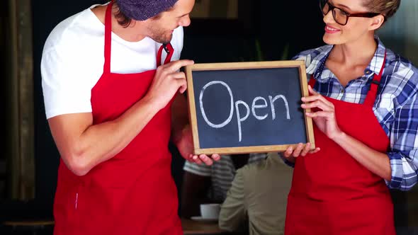 Smiling waiter and waitresses holding open sign board