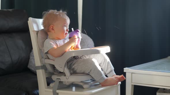 Cute Kid with Baby Straw Feeding Cup Sitting in Booster Seat One Year Old Toddler Watching Tv