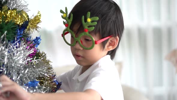 Asian Child Hanging Decorative Toy Together On Christmas Tree