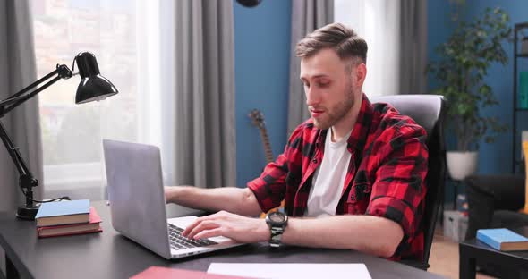 A Handsome College Student Boy is Studying Remotely While Sitting at a Desk in Living