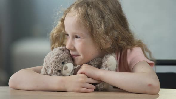 Happy Child Sitting at The Table, Holding Teddy Bear and Smiling. Childhood