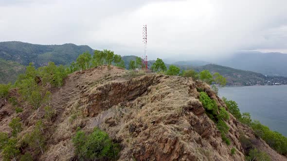 Aerial drone rising over a red and white telecommunications tower on top of a rocky mountain on the