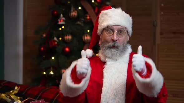 Portrait of Santa Claus Looking at Camera Listens Attentively and Makes a Thumbs Up Gesture