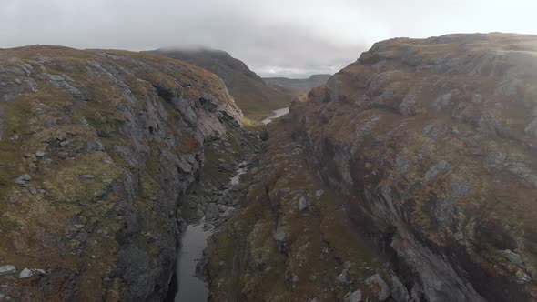 River flowing in canyon with dark clouds above, Norway highlands, rising aerial