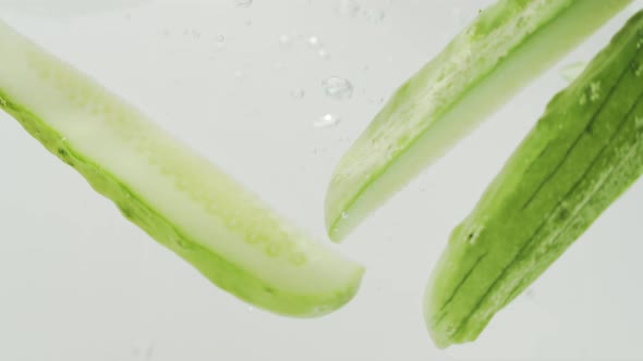 Cucumber Slices Falls Into The Water Inside A Glass Tank. - close up, studio shot
