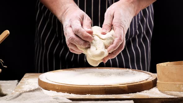 Chef in a black apron kneads a ball of white wheat flour dough 
