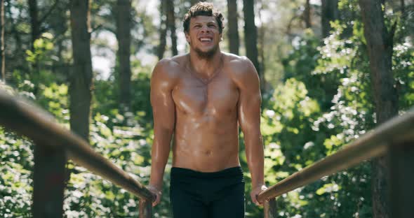 Strong Young Man Is Doing Triceps Dips on Parallel Bars. Exercising Outdoors in the Morning in