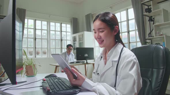 Young Asian Woman Doctor Is Using Tablet While Work With Computer In Workplace. Medical Concept