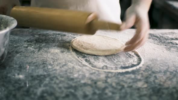 Closeup Male Hands Roll Out Pastry with Wooden Rolling Pin on a Stone Table