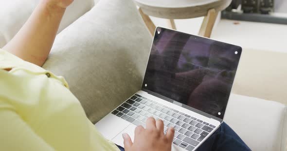 Video of plus size african american woman sitting on sofa with laptop with copy space