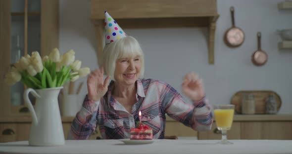 Cheerful Senior Woman Celebrates Birthday Alone with Piece of Cake and Candle. 70s Woman in Birthday