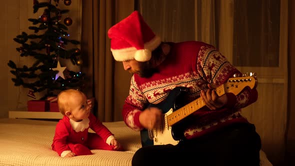 Father in Santa Hat and Christmas Sweater Playing Guitar to Little Child