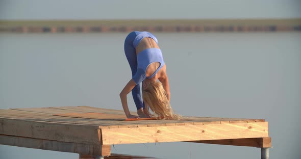 Yoga Outdoors By a Young Blonde Woman on a Wooden Platform on the Lake