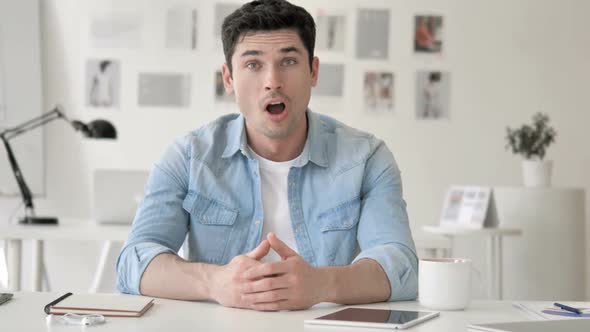 Casual Young Man in Shock Sitting at Workplace