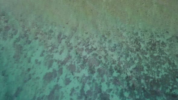 Beautiful aerial bird's eye view of clear shallow water tilting up to reveal the small rural coastal