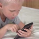 The boy lies on the bed with a smartphone in his hands. - VideoHive Item for Sale
