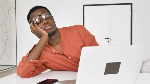 Sleepy AfricanAmerican Man Awakes Near Laptop at Table