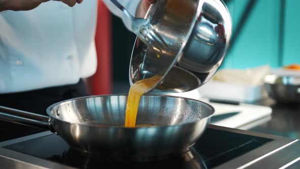 Professional restaurant kitchen, close-up: Chef pouring eggs into a frying pan, preparing an omelet