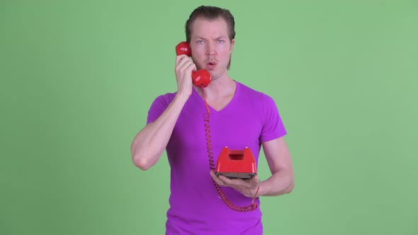 Confused Young Man Using Old Telephone and Shrugging Shoulders