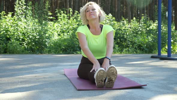 Mature Woman Does Body Stretching Workout on Mat in Park