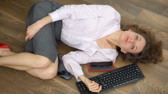 Tired Young Female Office Manager is Lying on the Floor with Keyboard Mouse and Smartphone Lay Flat