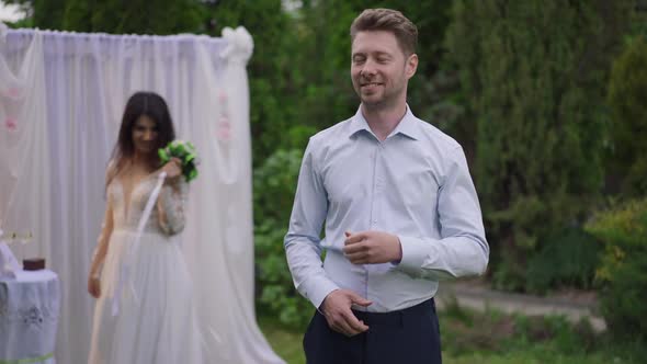 Confident Proud Caucasian Man Posing on Marriage Ceremony Looking Back at Happy Middle Eastern Woman