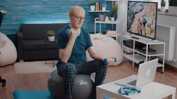 Senior Man Sitting on Toning Ball and Using Dumbbells