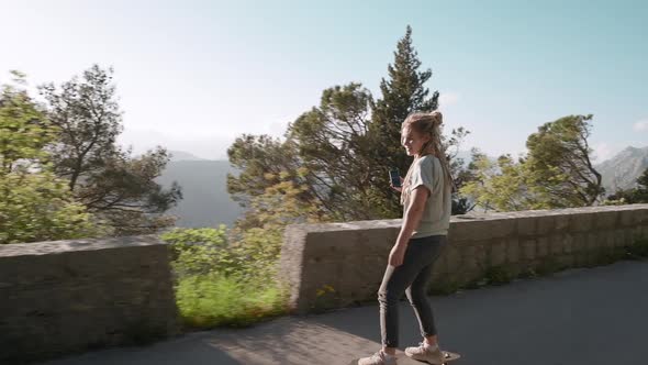 Happy dreadlocks woman with smartphone longboarding on mountain background